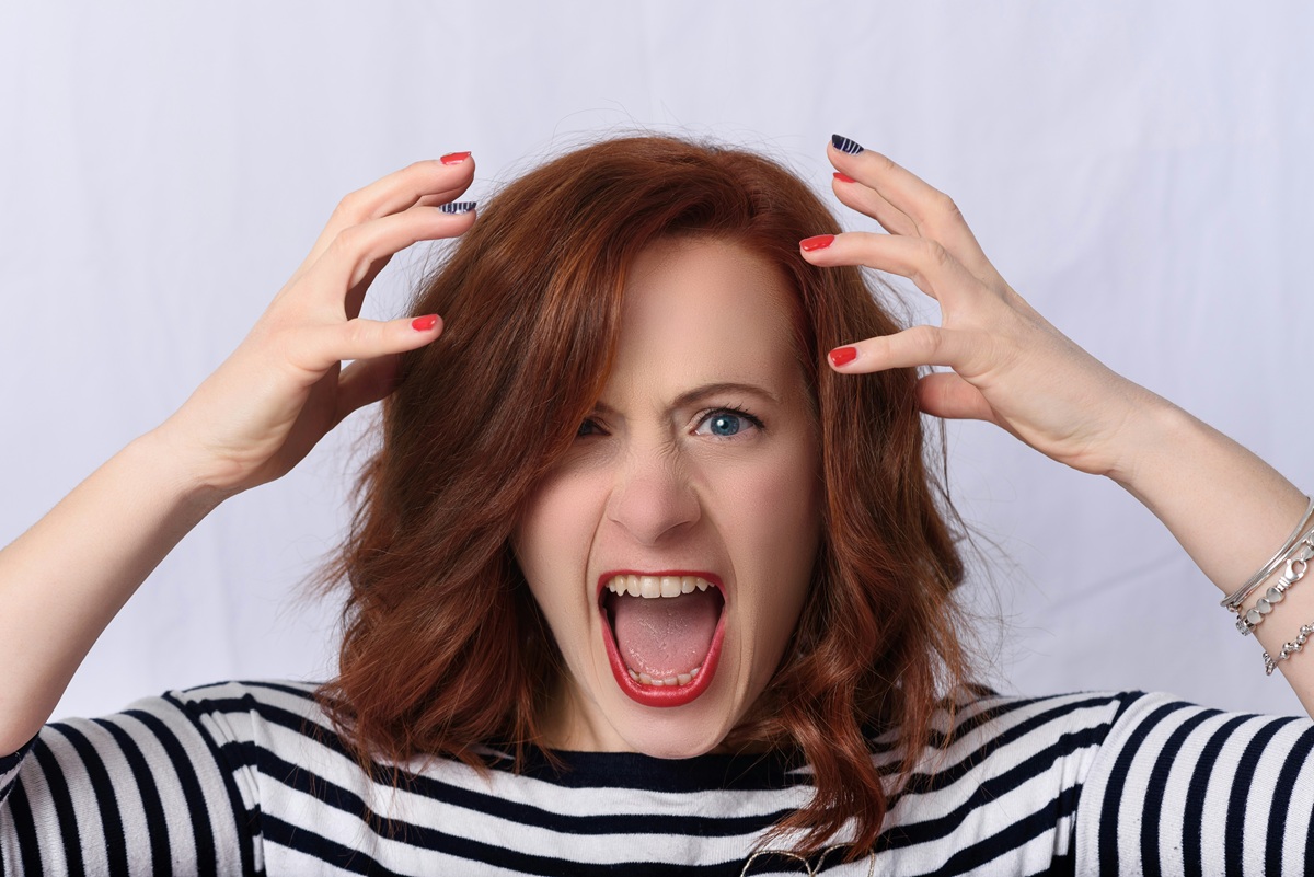 A woman expressing visible frustration, holding her head and shouting.